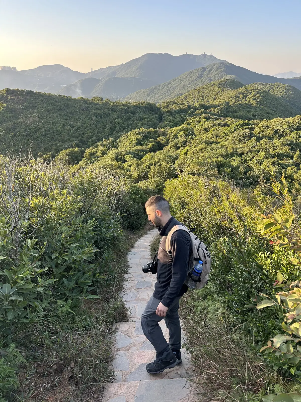 Nir walking down a stone trail through green hills in Hong Kong